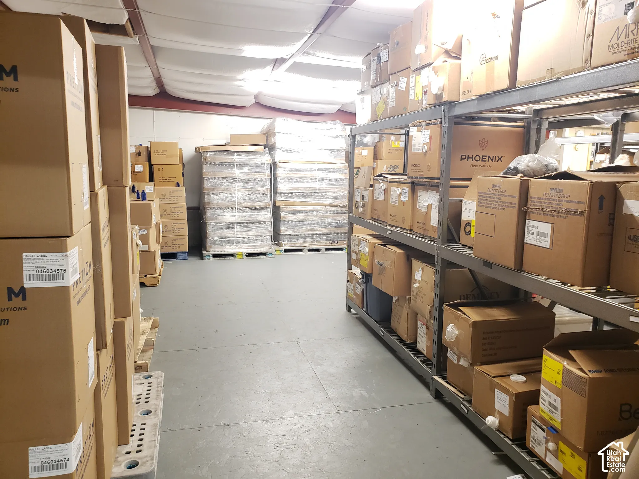 Industrial storage space featuring reinforced metal shelving units, concrete flooring, and an exposed steel-truss ceiling with insulation
