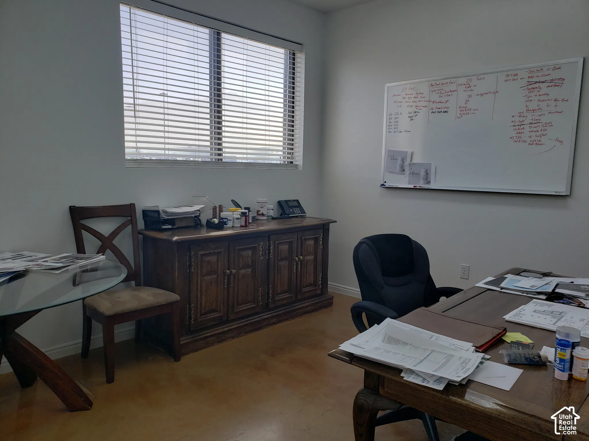 Room featuring polished concrete flooring, a large window with horizontal blinds, and a wall-mounted whiteboard