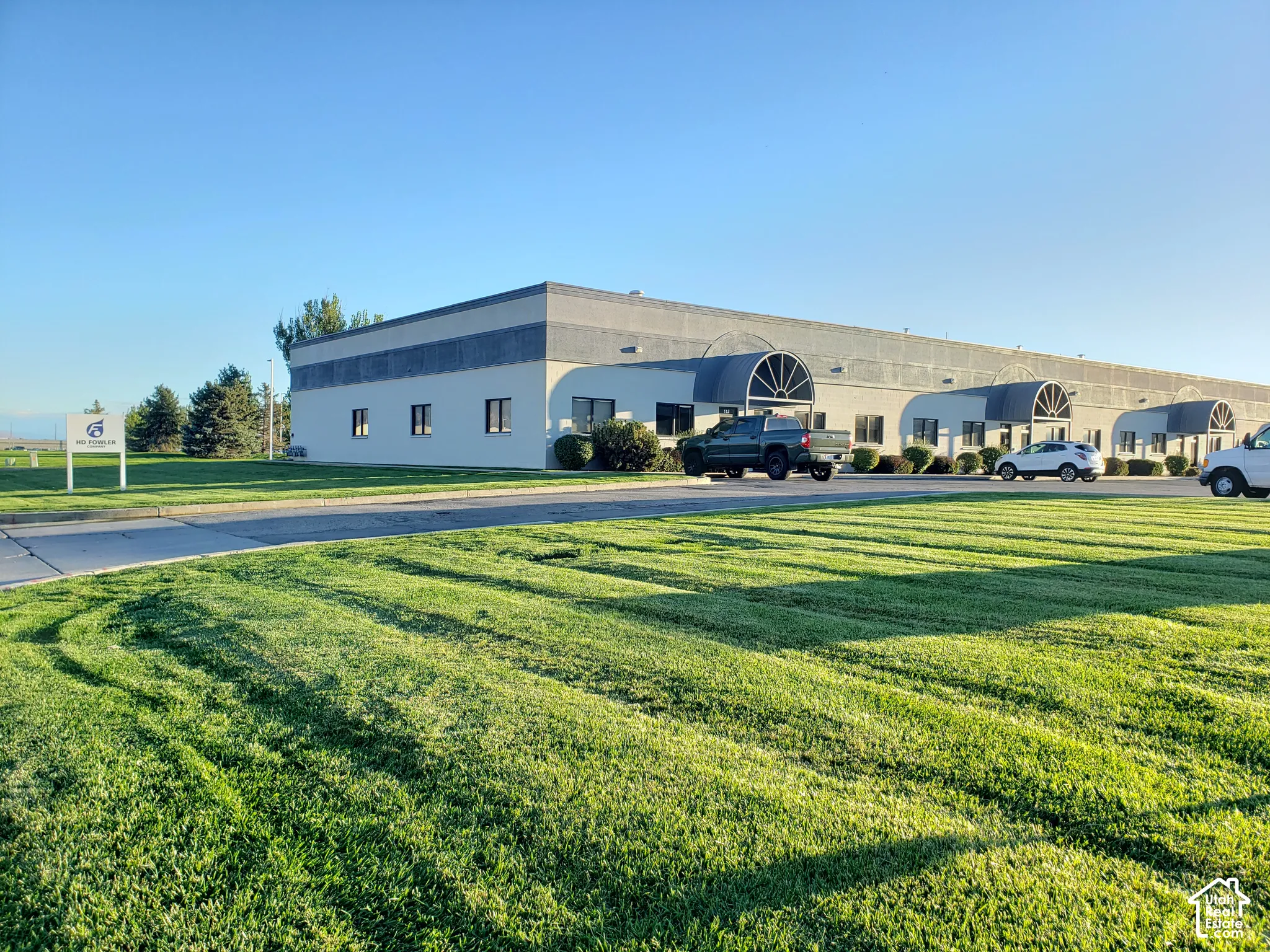 Commercial building exterior featuring a low-profile concrete facade, multi-bay entrance awnings with arched metal detailing, and an expansive paved parking surface