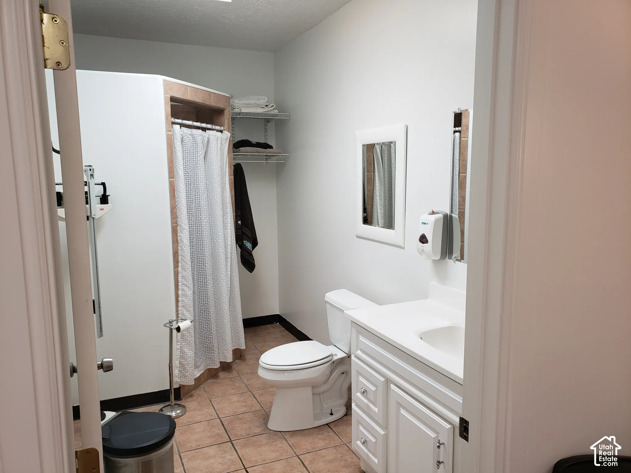 Bathroom featuring a tiled shower enclosure, white vanity cabinet with integrated sink, ceramic tile flooring, and wall-mounted shelving