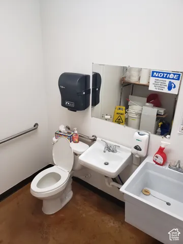 Restroom featuring a wall-mounted sink, separate utility basin, polished concrete flooring, and stainless steel grab bars