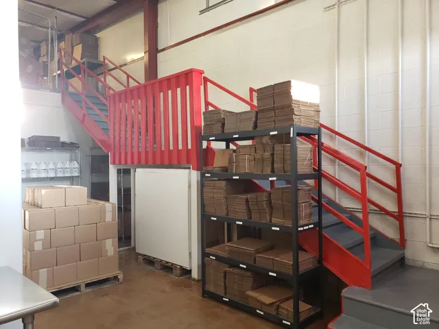 Industrial space featuring high ceilings, painted masonry walls, steel structural beams, and a red-finished metal staircase