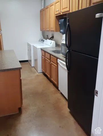 Kitchen area featuring wooden cabinetry, dark-finish refrigerator, integrated dishwasher, solid surface countertops, and concrete flooring