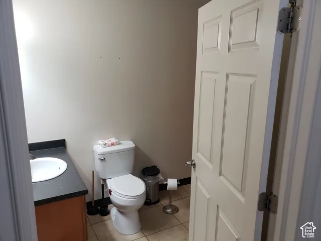 Bathroom featuring a vanity with a dark countertop and integrated sink, a porcelain toilet, and neutral tile flooring