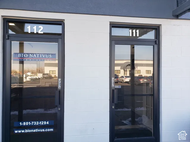 Exterior facade featuring white concrete block walls, dark metal-framed glass doors, and transom windows with numerical signage