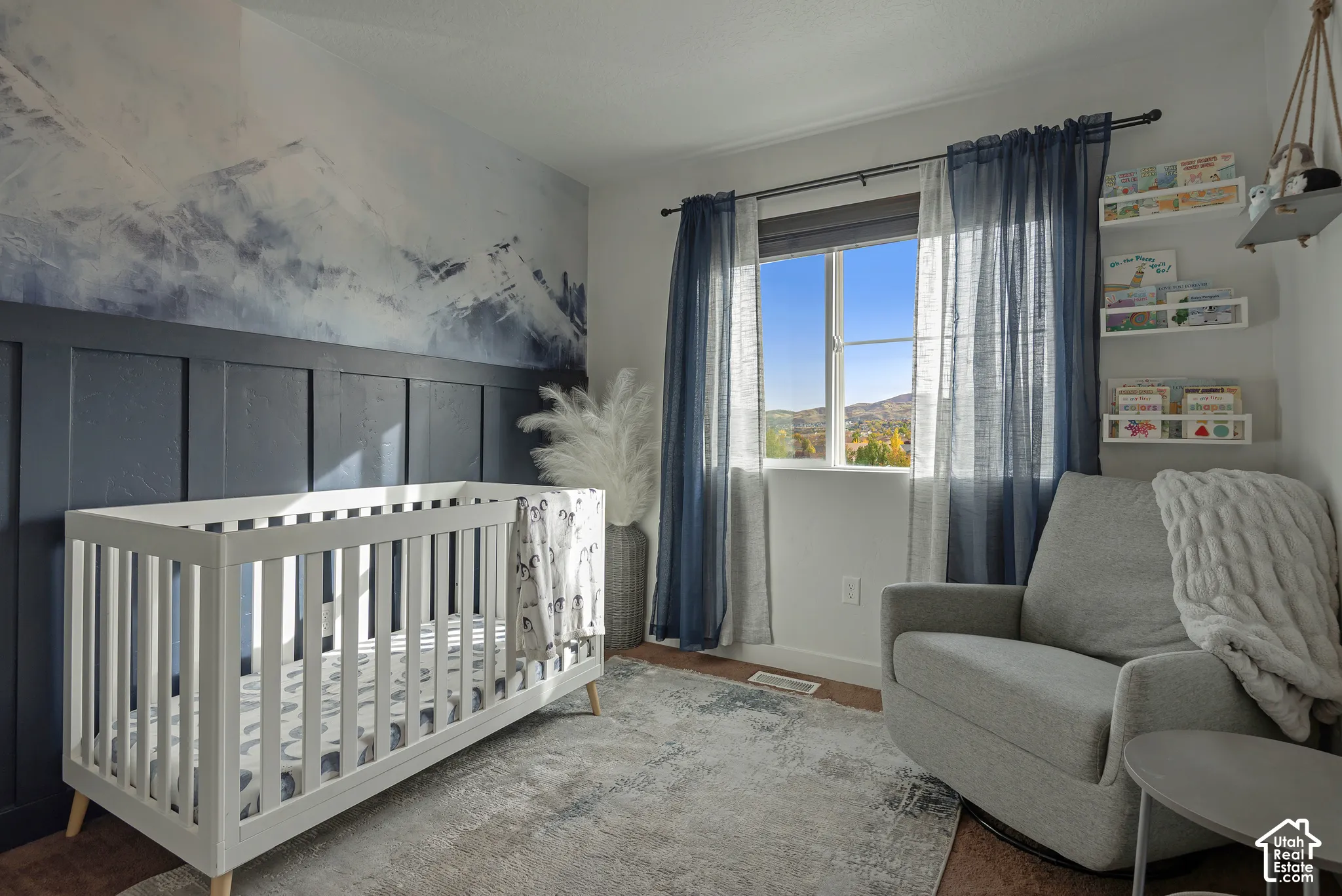 Room featuring dark-toned board and batten wainscoting, mountain-themed mural, and three built-in wall shelves