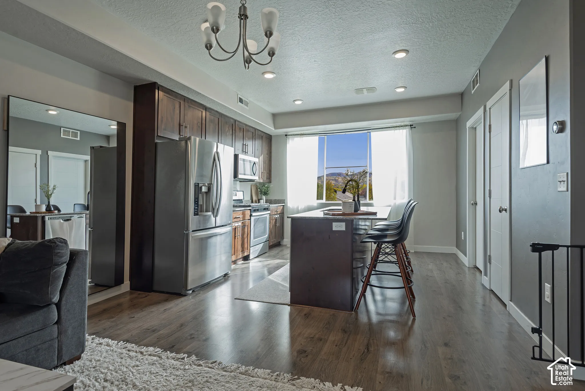 Kitchen featuring dark-toned cabinetry, stainless steel appliances, a central island with counter seating, and wood-finish flooring