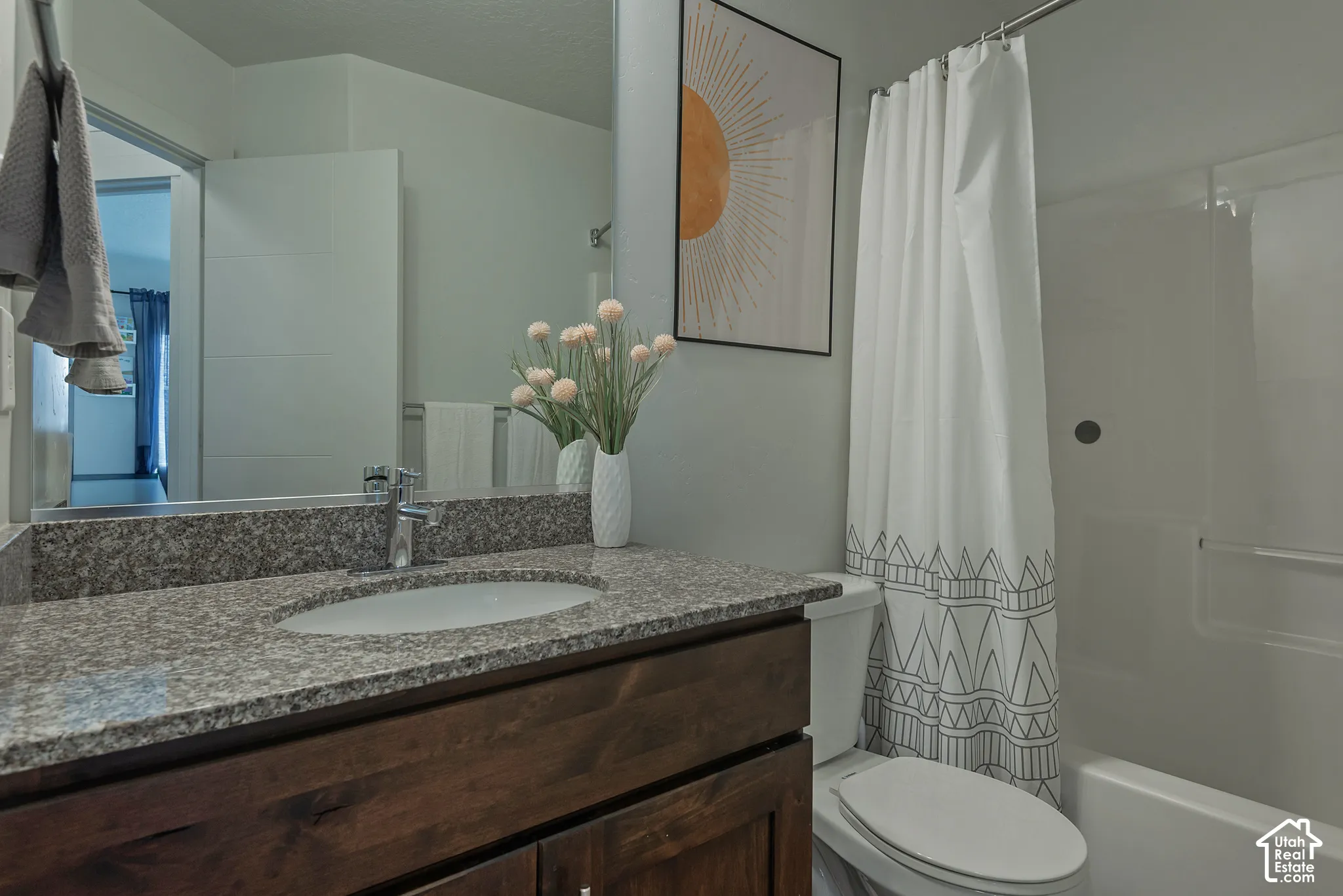 Bathroom featuring a vanity with dark wood-finish cabinetry, stone-composite countertop with an integrated oval sink, full-width wall mirror, and a tub-shower combination with a surround enclosure