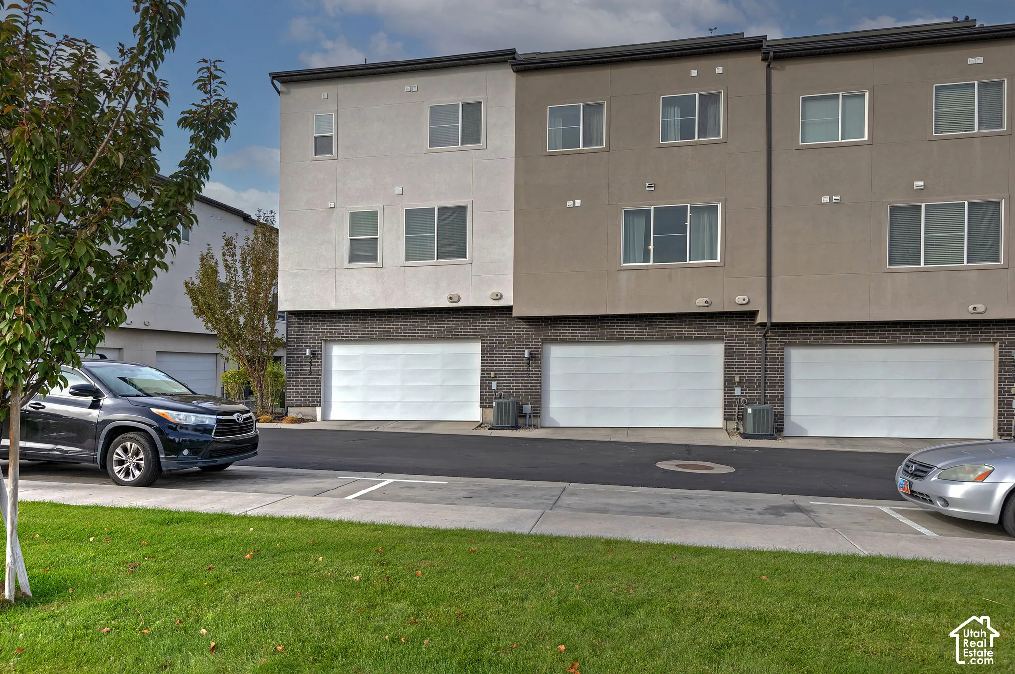 Three-story townhome exterior featuring a combination of stucco and dark brick facade, multi-level windows, and attached two-car garages