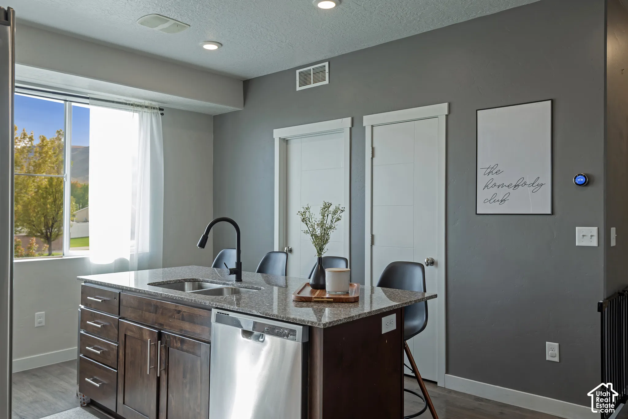 Kitchen island with a stone-composite countertop, dark wood-finish cabinetry, stainless steel dishwasher, and a matte black gooseneck faucet