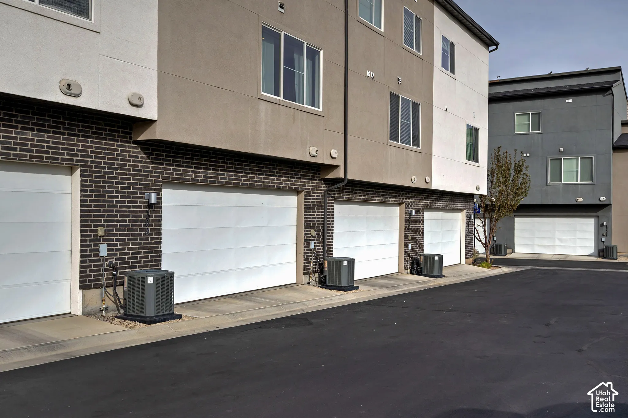 Multi-level exterior featuring dark brick masonry, smooth-finish siding, white sectional garage doors, and individual HVAC condenser units