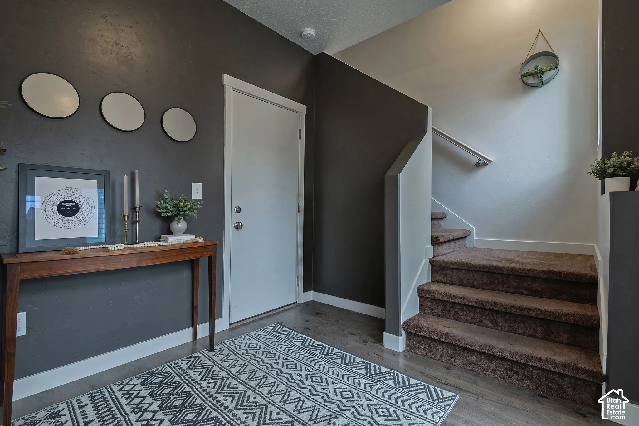 Entryway featuring dark-toned walls, wood-finish flooring, and a staircase with carpeted treads and a metal handrail