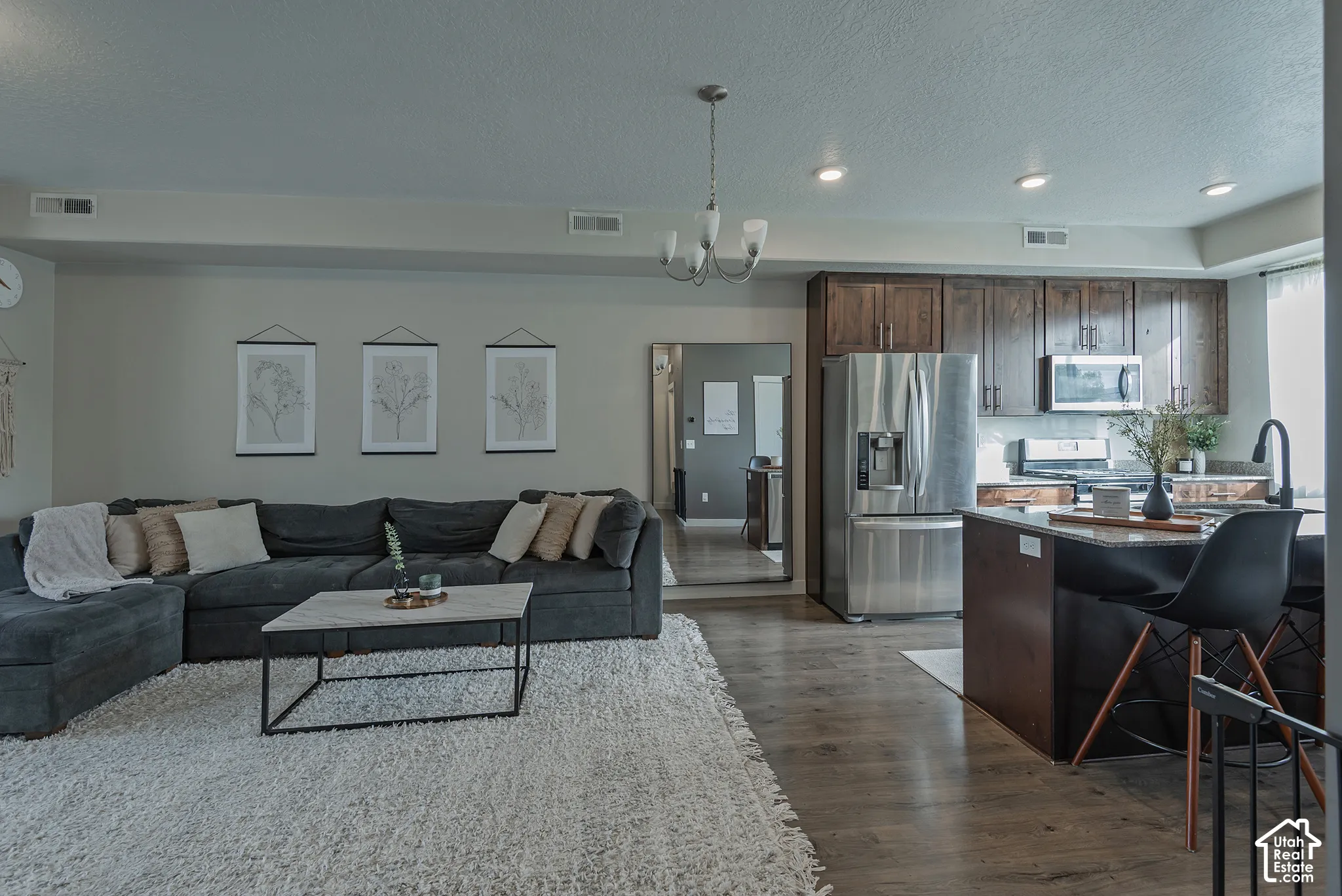 Open-concept living space featuring wood-finish flooring, dark wood cabinetry, stainless steel appliances, stone-surface kitchen island, and recessed lighting