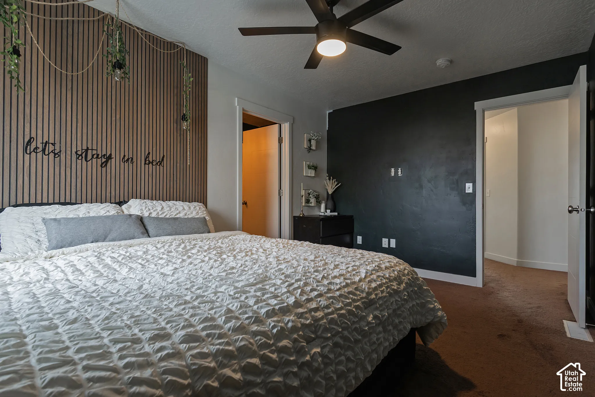 Bedroom featuring a slat-style wood accent wall, a matte black ceiling fan with integrated lighting, and a contrasting dark-toned accent wall