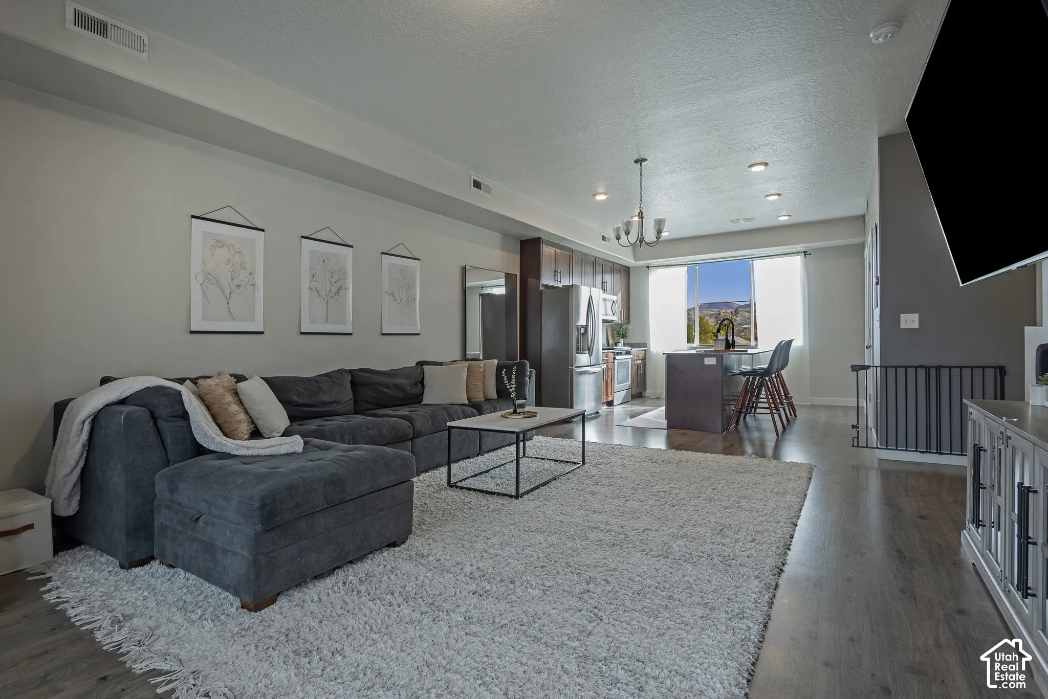 Open-concept main room featuring wood-finish flooring, recessed lighting, a multi-light chandelier, and a kitchen island with stone-surface countertops
