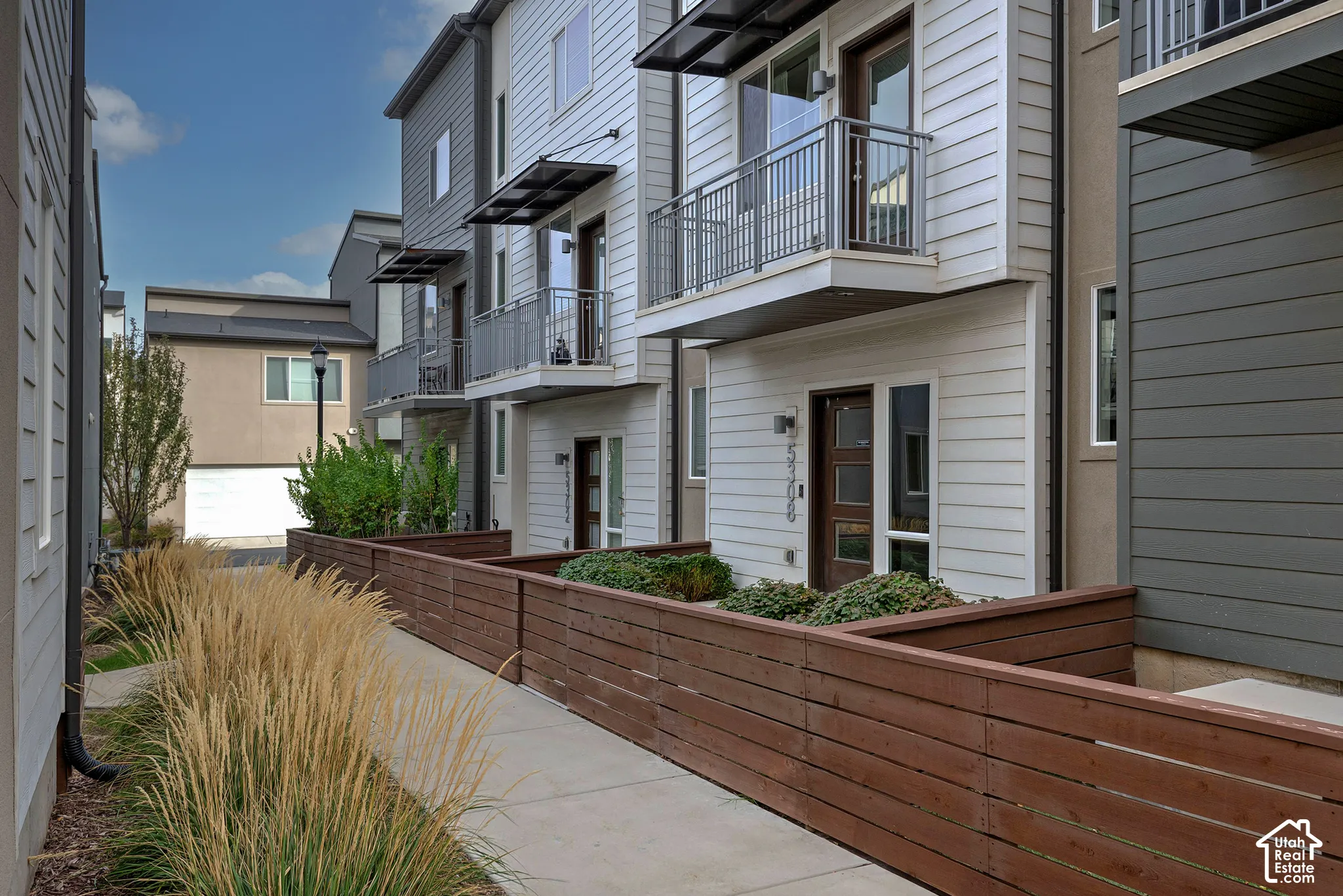 Multi-story exterior featuring horizontal lap siding, metal balcony railings, horizontal wood fencing, and metal door awnings