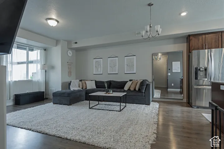 Open-concept area featuring wood-finish flooring, recessed lighting, a multi-arm chandelier, and stainless steel refrigerator with built-in cabinetry