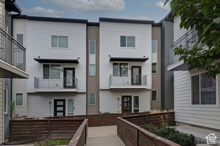 Multi-level exterior featuring white horizontal siding, contrasting dark-toned stucco accents, second-story balconies with metal railings, and wood-slat fencing