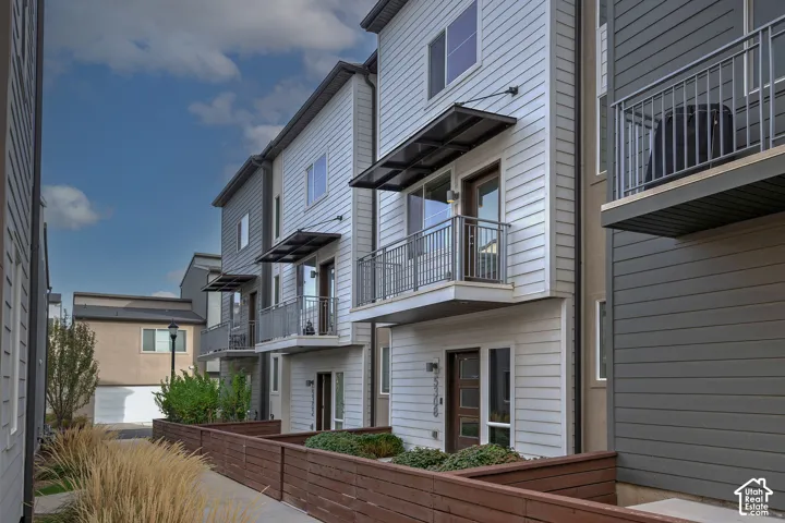 Multi-story townhome exterior featuring horizontal lap siding, metal-railed private balconies, contemporary awnings, and fenced front courtyards