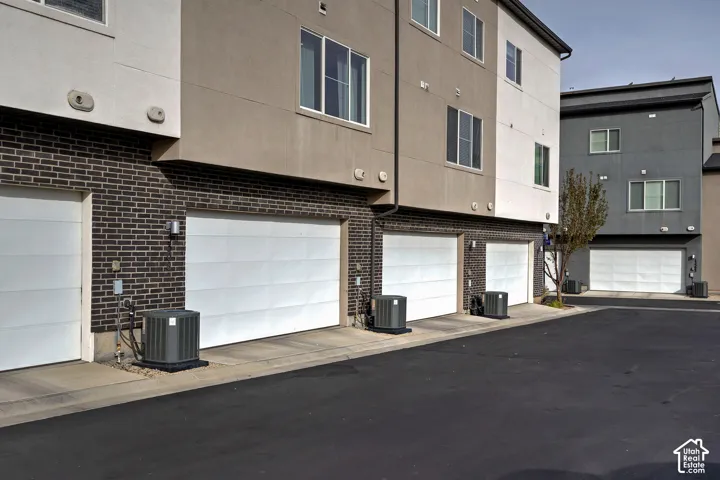 Multi-level exterior featuring dark brick masonry, smooth-finish siding, white sectional garage doors, and individual HVAC condenser units