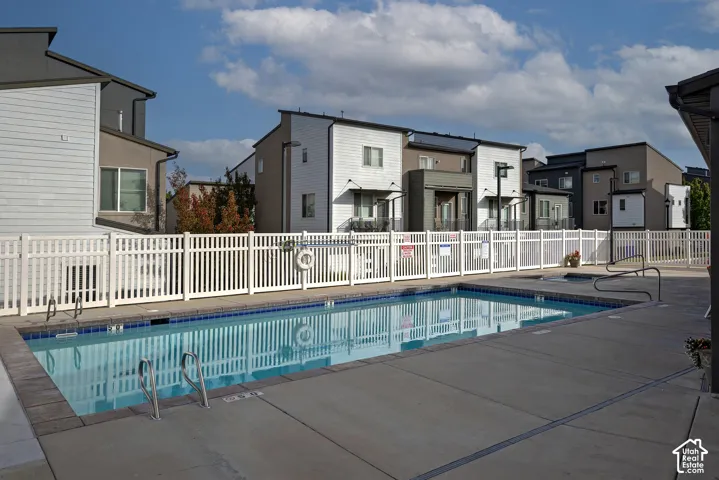 Rectangular swimming pool with metal ladder, concrete decking, and white vinyl perimeter fencing