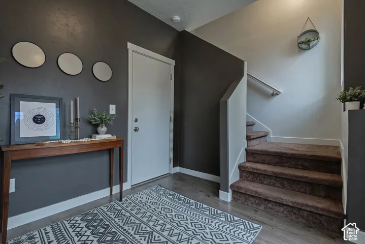 Entryway featuring dark-toned walls, wood-finish flooring, and a staircase with carpeted treads and a metal handrail