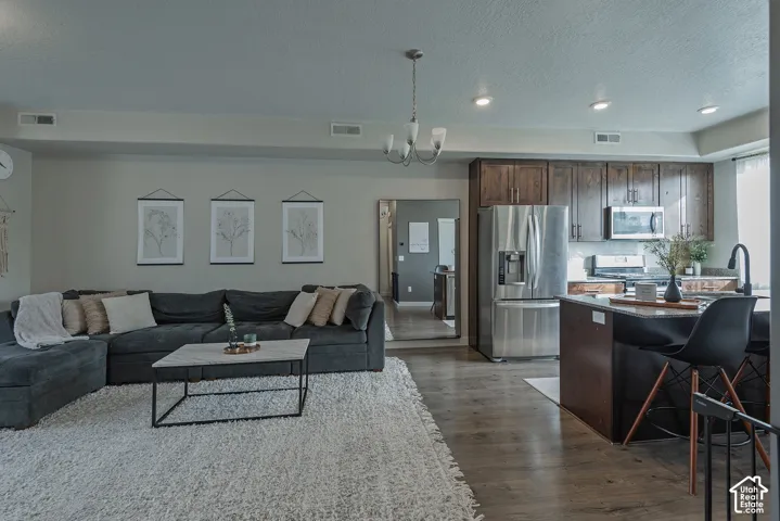 Open-concept living space featuring wood-finish flooring, dark wood cabinetry, stainless steel appliances, stone-surface kitchen island, and recessed lighting