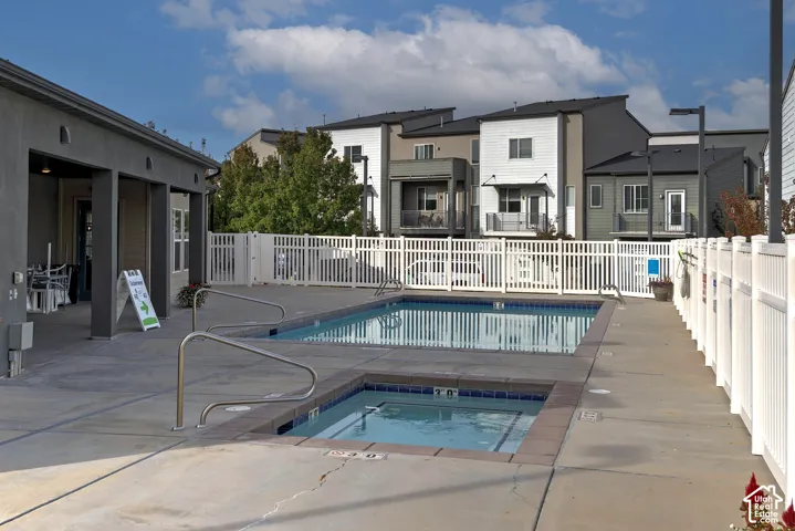 Outdoor swimming pool and spa area featuring concrete decking, metal safety railings, and perimeter vinyl fencing