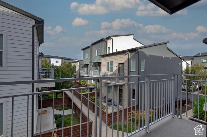 Private balcony featuring metal railings and concrete flooring, overlooking a residential exterior with horizontal siding, multi-toned facades, and fenced ground-level outdoor spaces