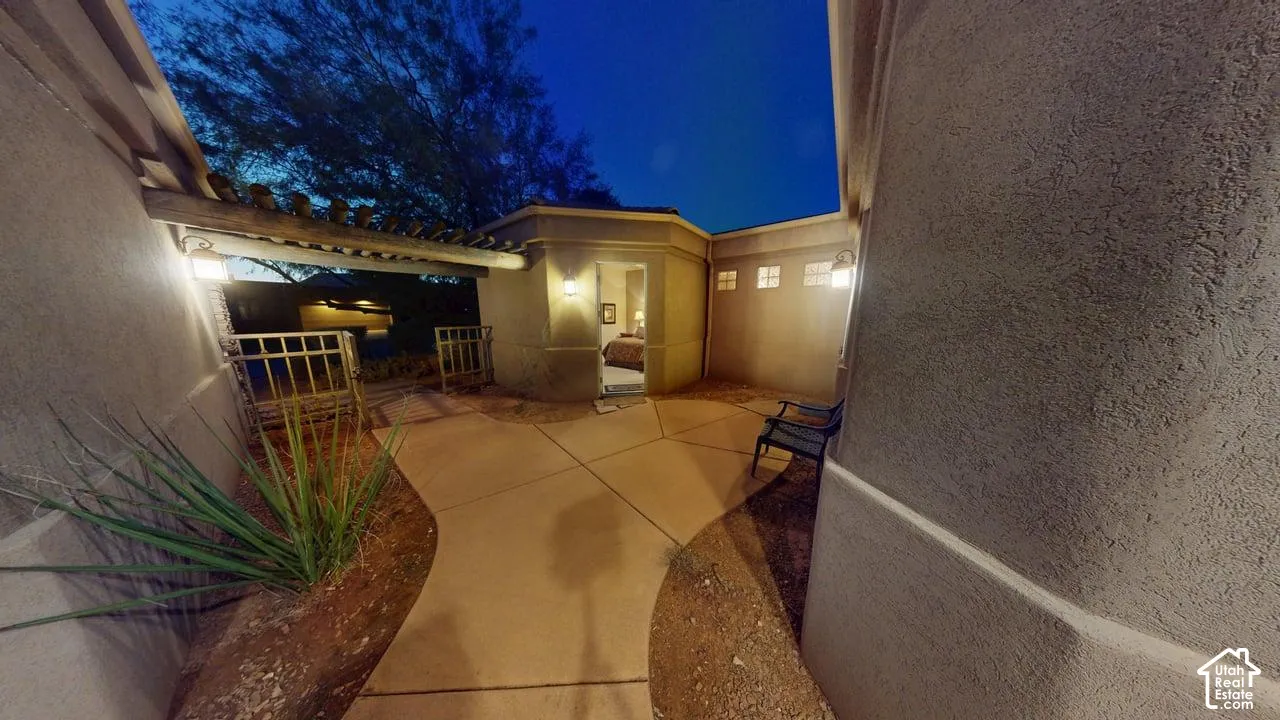 Stucco courtyard entry featuring a concrete patio, wood-beam pergola, integrated wall sconces, and xeriscaped ground cover