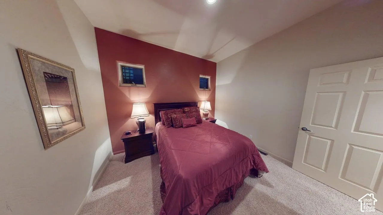 Room featuring vaulted ceilings, neutral carpeting, a painted accent wall, and dual high-set windows