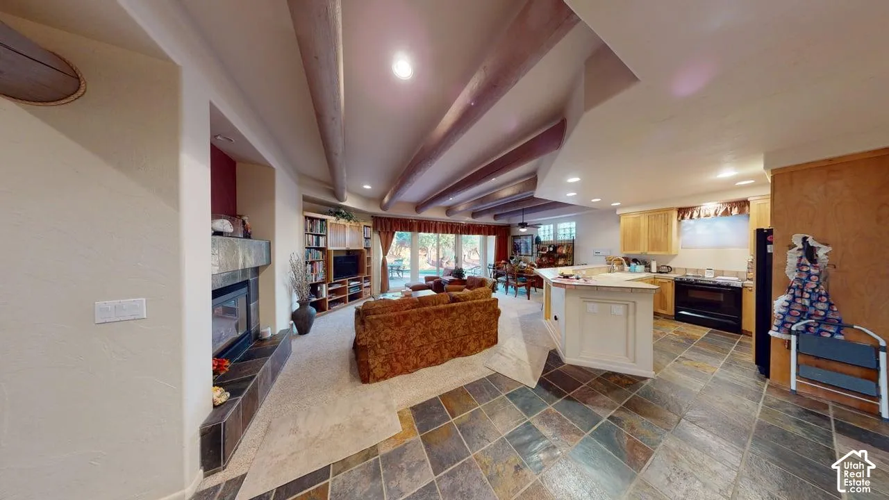Open floor plan featuring exposed wood ceiling beams, natural stone tile flooring, a built-in stone-surround fireplace, and a kitchen island with stone countertops