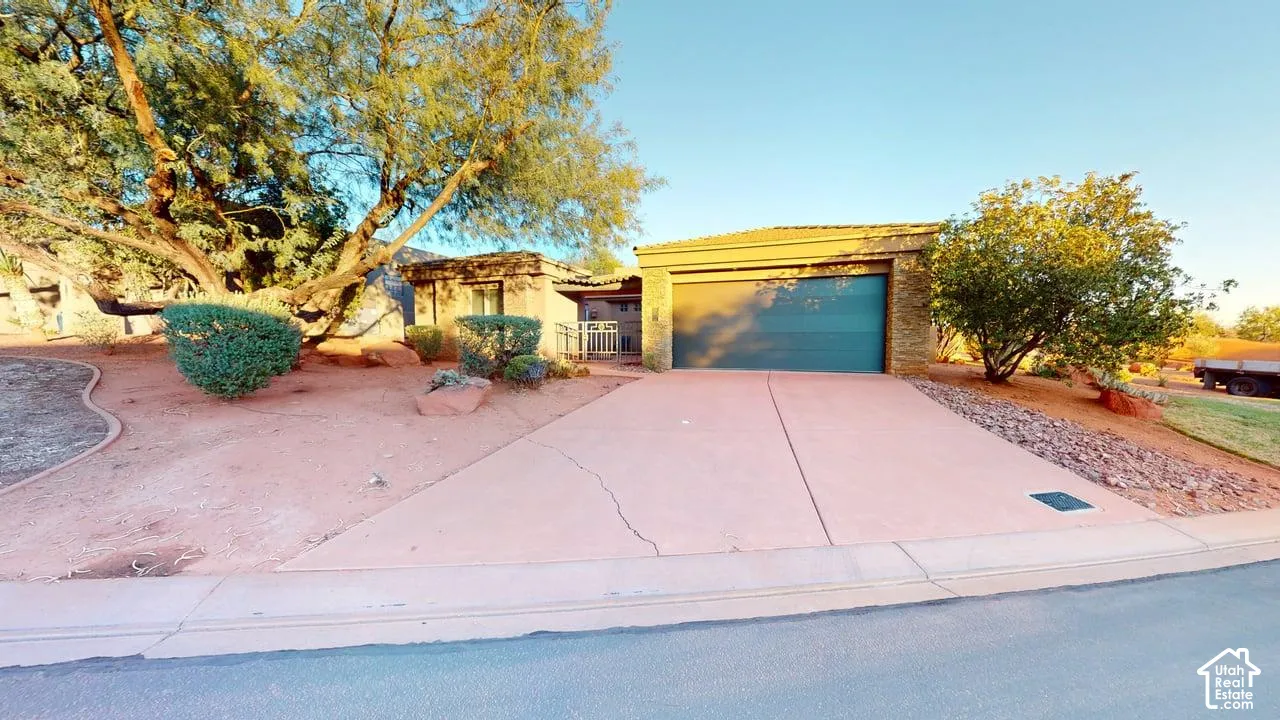 Stucco exterior featuring a two-car garage, concrete driveway, and natural desert landscaping