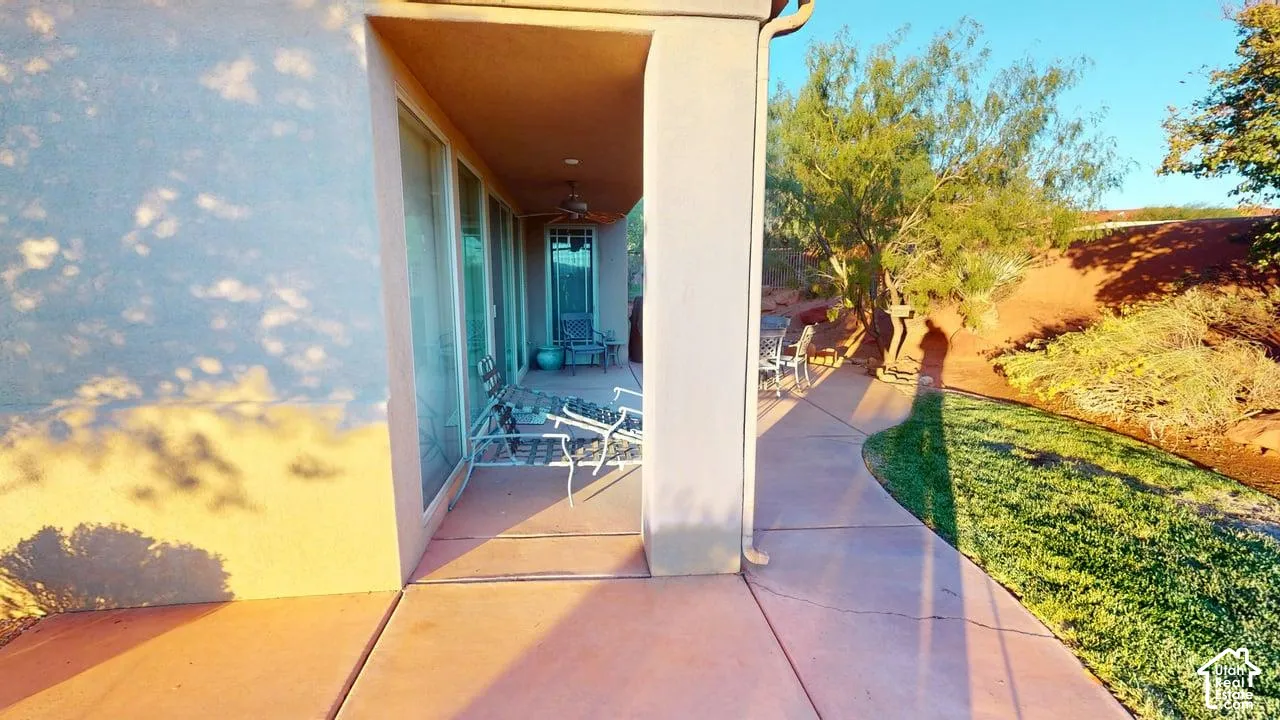 Covered concrete patio featuring a ceiling fan, sliding glass door access, and xeriscaped landscape surroundings