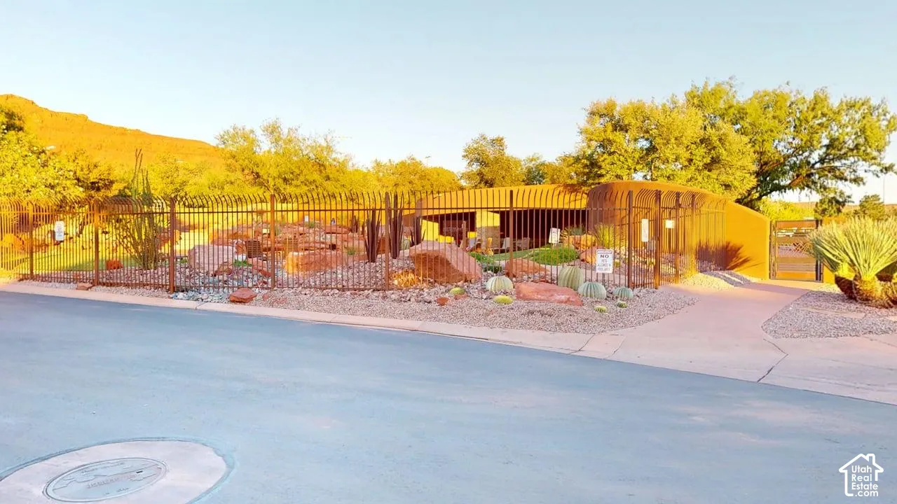 Stucco exterior featuring curvilinear architecture, metal perimeter fencing, xeriscaped rock garden, and desert flora