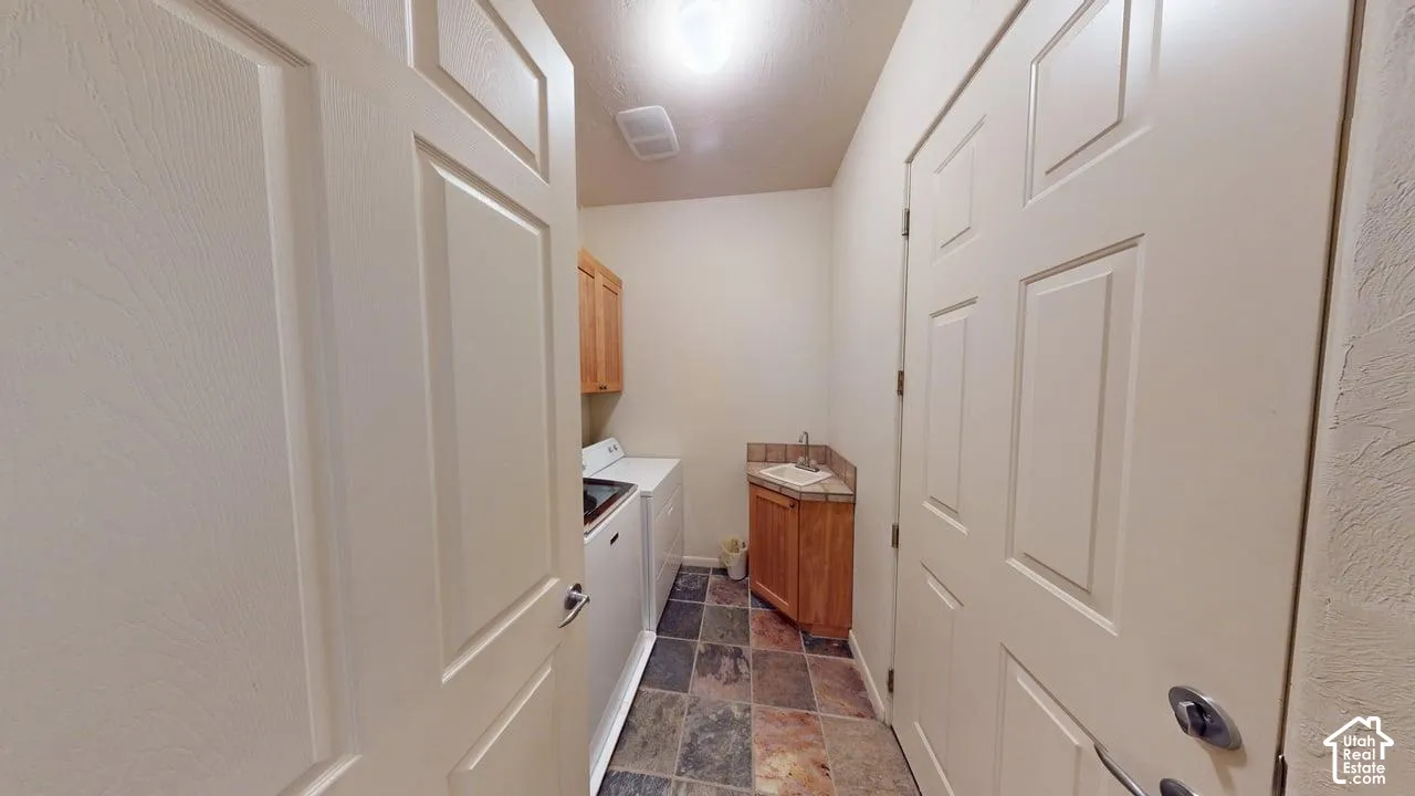 Laundry area featuring multi-tonal stone flooring, wooden cabinetry, and a corner sink with a tile backsplash