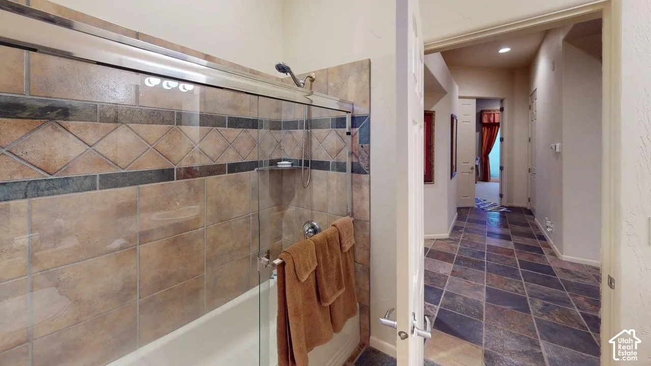 Bathroom featuring a tub-shower combination with glass enclosure, decorative tile surround with diamond-pattern accents, and stone-finish floor tiles