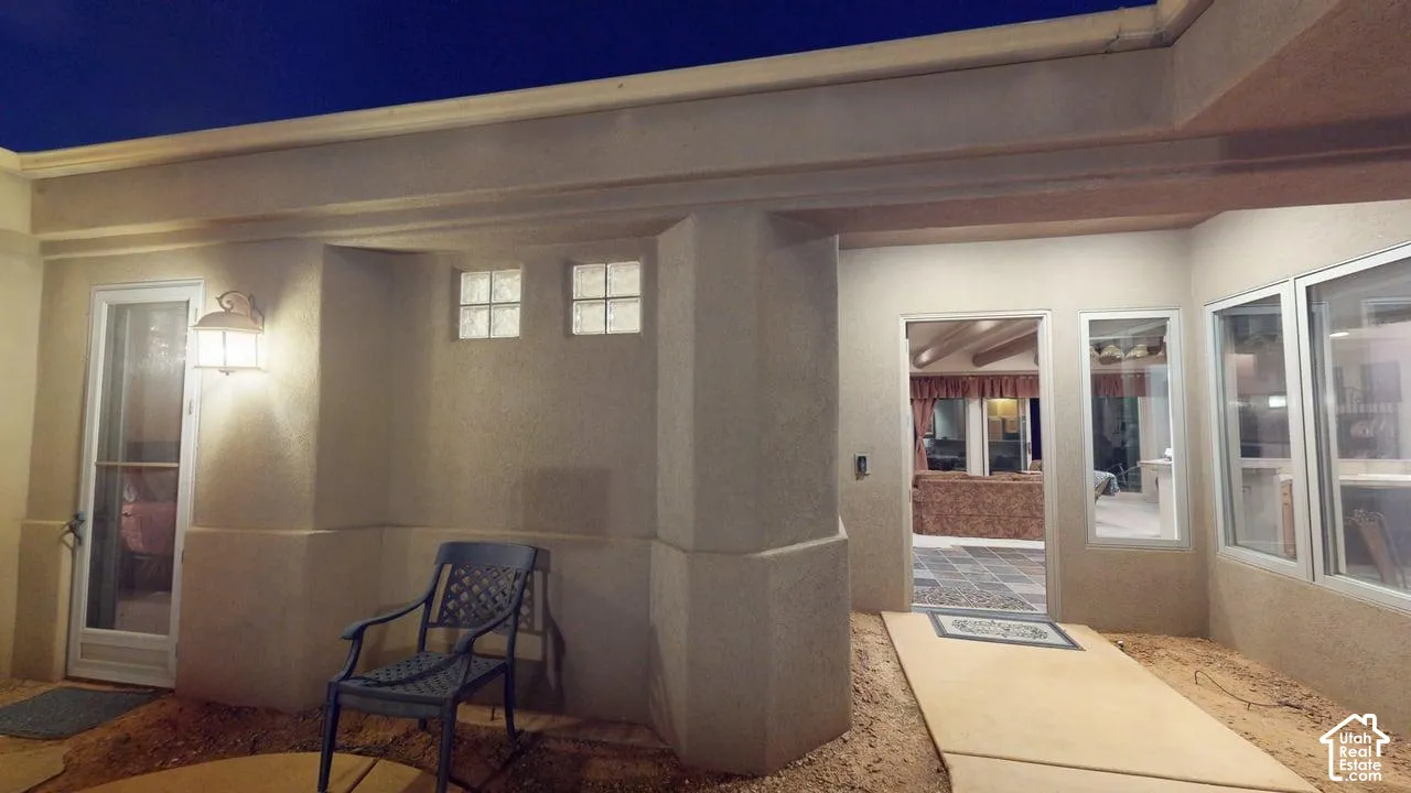 Stucco exterior entry featuring a covered patio, inset glass block windows, and wall-mounted exterior lighting