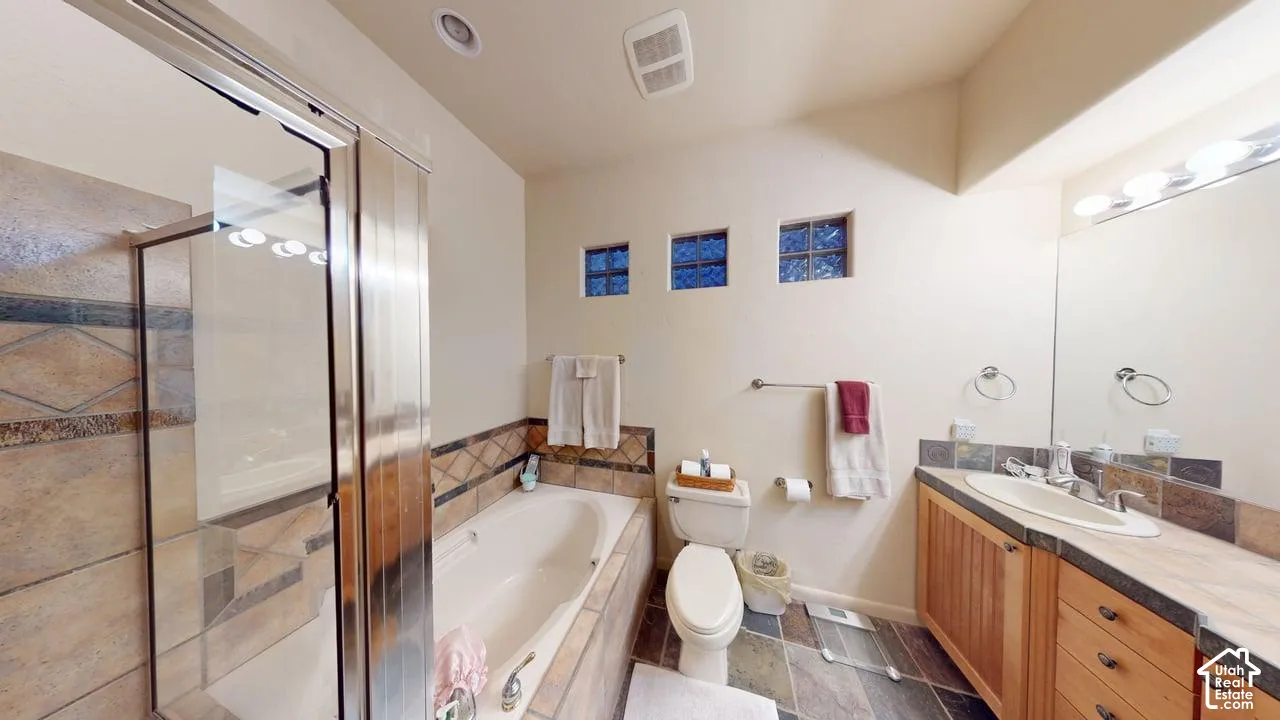 Bathroom featuring a stone-tiled soaking tub, a separate glass-enclosed shower, natural-tone wood cabinetry, an integrated vanity sink, and multiple high-set square windows