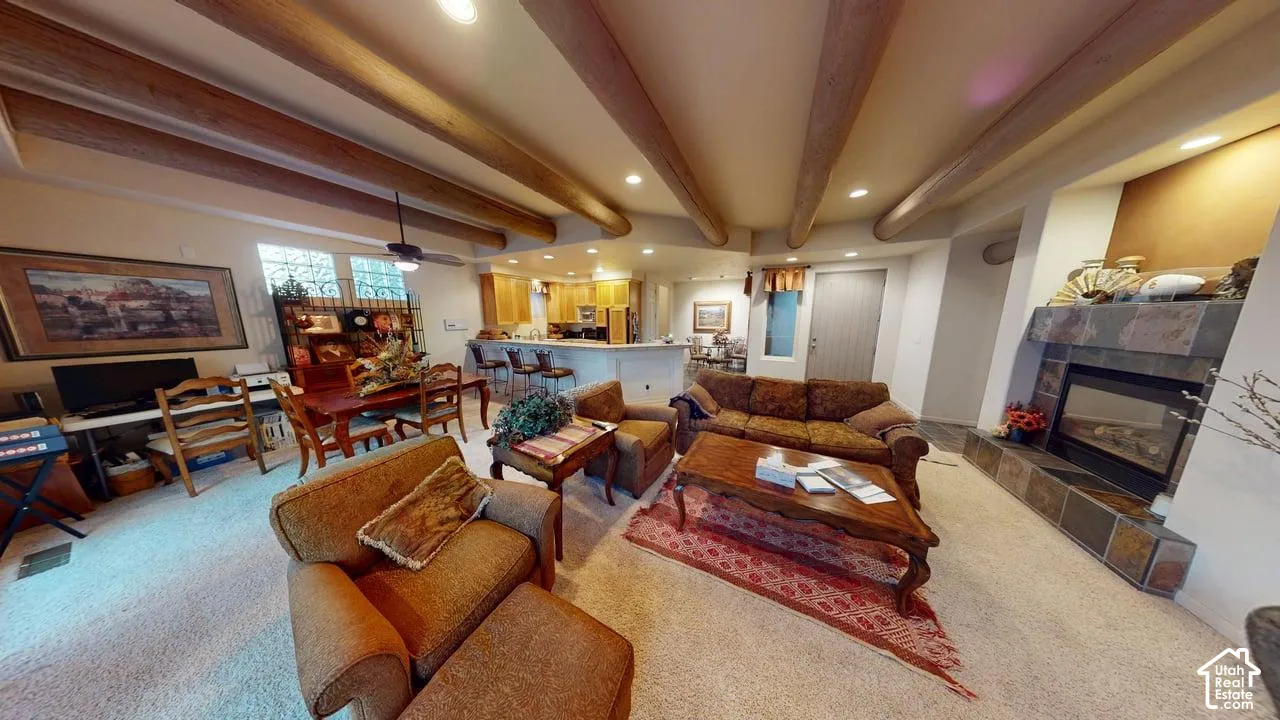 Exposed wood ceiling beams, tiled fireplace surround, recessed lighting, and kitchen peninsula with bar seating
