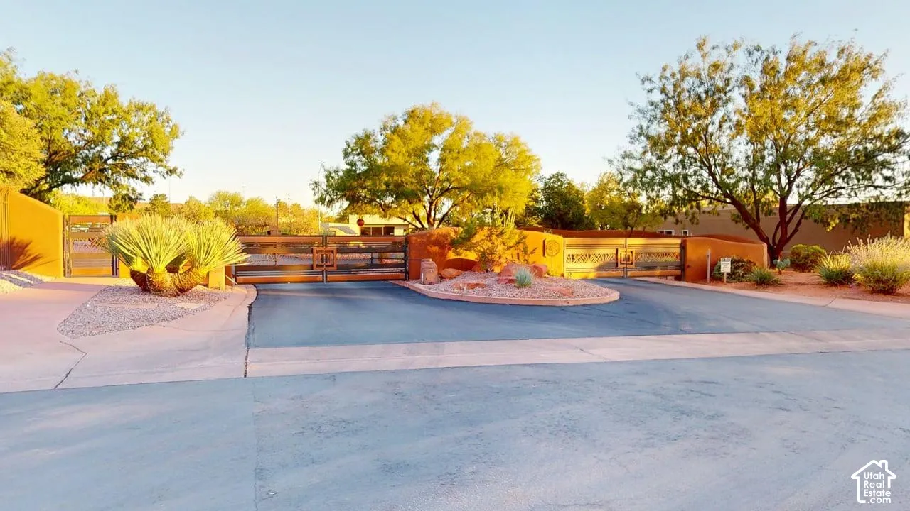 Gated entrance featuring stucco perimeter walls, metal security gates, paved driveway, and desert landscaping