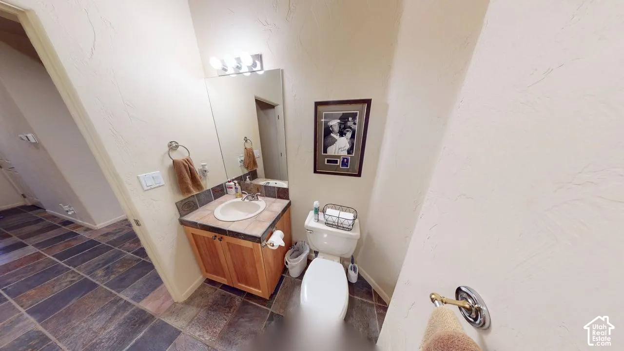 Bathroom featuring a wooden vanity, tile-surround countertop with an integrated basin, large wall-mounted mirror, four-light vanity fixture, and slate-tile flooring