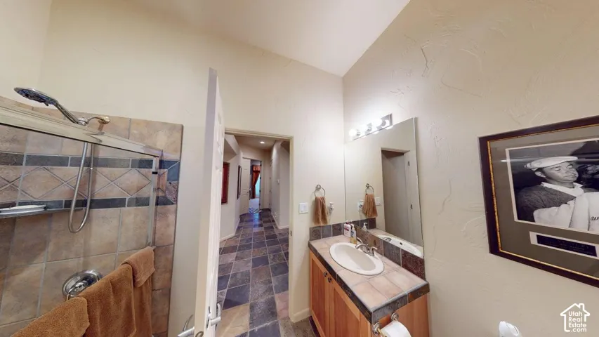 Bathroom featuring tile flooring, a wood-finish vanity with an inset sink, tile-surround shower with a metallic fixture, and a wall-mounted mirror
