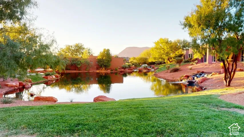 Water feature bordered by natural stone, manicured lawn, and mature trees with a mountain backdrop