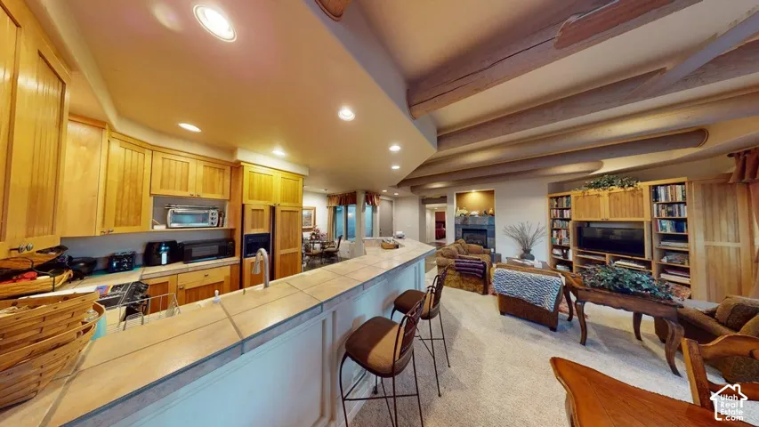 Kitchen featuring natural wood cabinetry, tile countertops, built-in shelving, and exposed ceiling beams