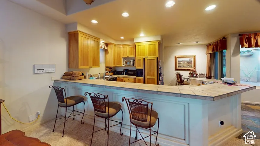 Kitchen featuring custom natural wood cabinetry, a breakfast bar with tiled countertops, and recessed lighting