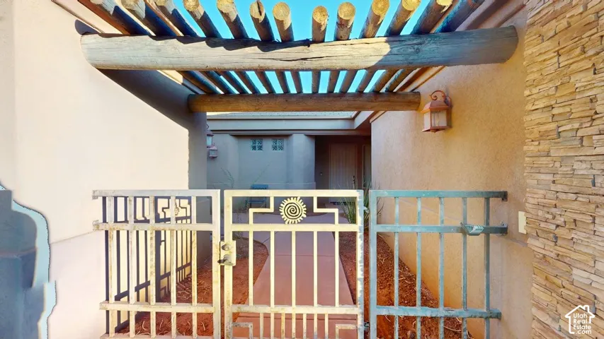 Courtyard entrance featuring a decorative metal gate, stacked stone masonry, and a rustic log-beam pergola