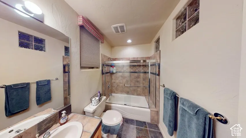 Bathroom featuring tile flooring, a tiled shower surround with a glass enclosure, a vanity with an integrated basin, and glass block accent windows