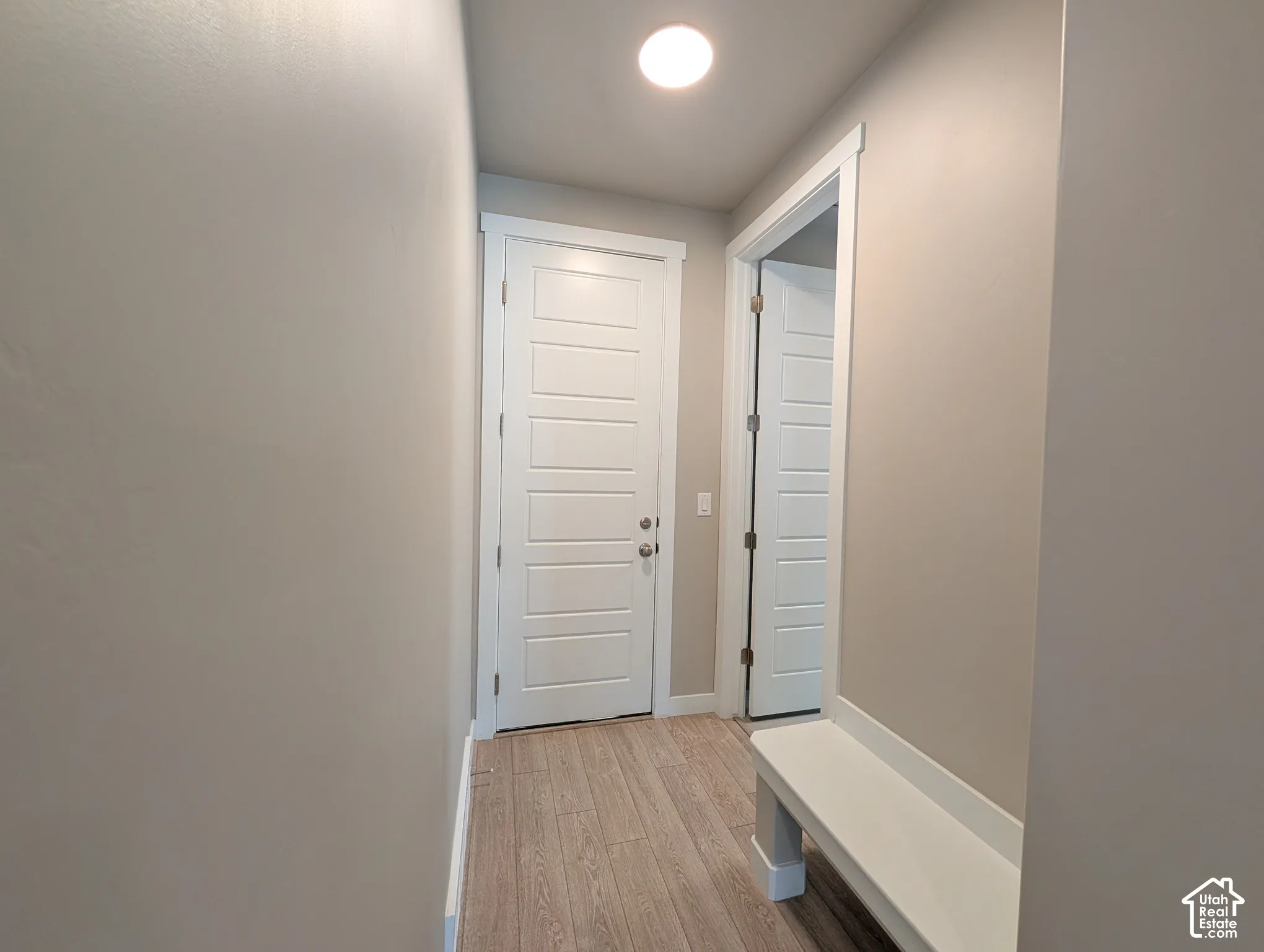 Neutral wall paint, wood-finish flooring, recessed ceiling lighting, and white five-panel interior doors with a built-in white bench