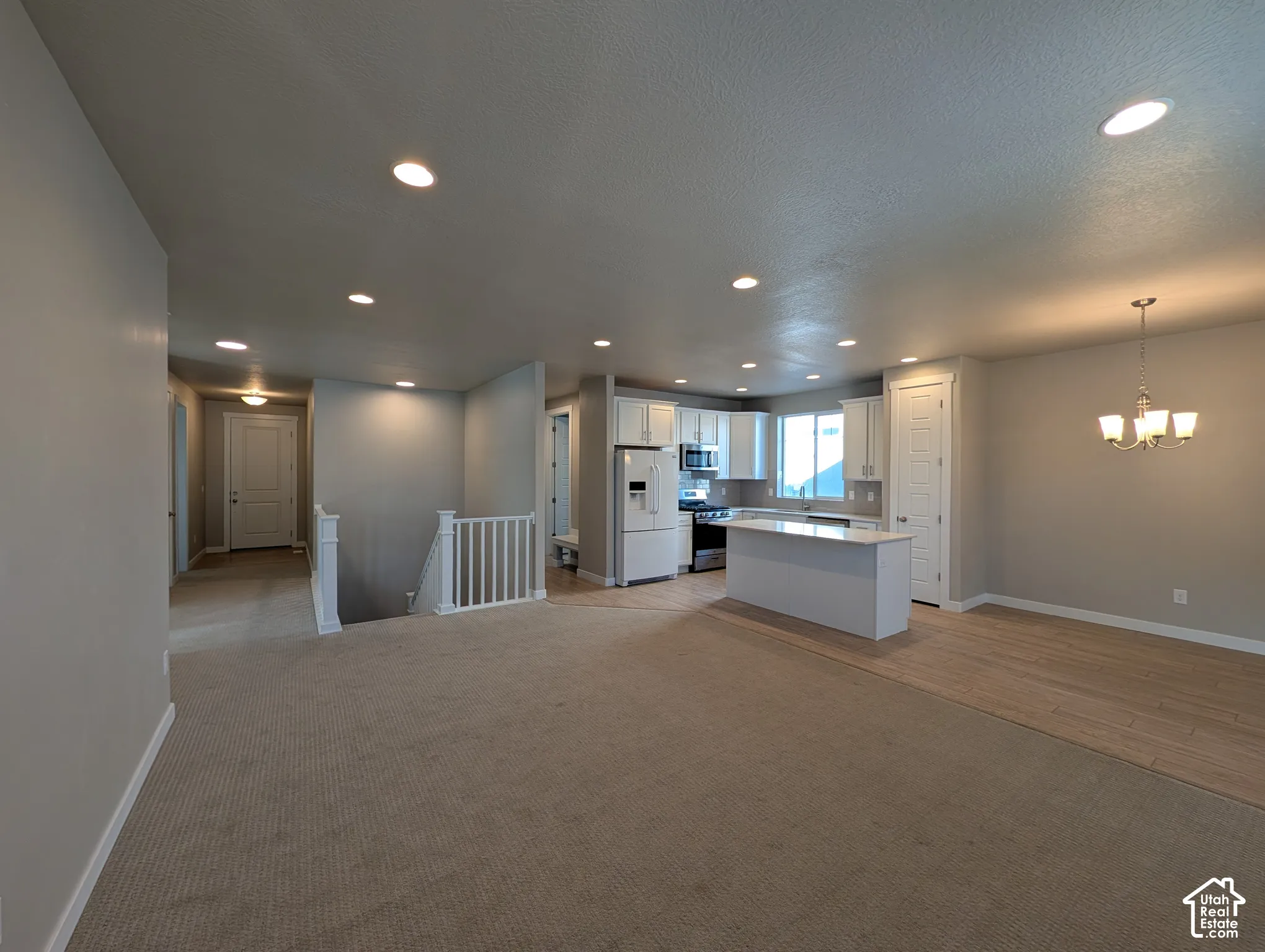 Open-concept floor plan featuring recessed lighting, a kitchen island with stone countertops, wood-finish flooring, and a multi-tiered chandelier